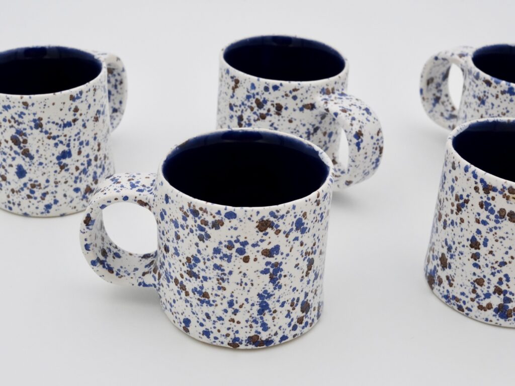 Tasses en céramique artisanale effet granito de la collection Brutalism, émail blanc moucheté à l’extérieur et bleu profond à l’intérieur.